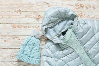 Kışlık ceket, süveter ve hafif ahşap arka planda örülmüş şapka.