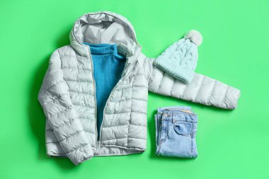 Kış ceketi, kazak, örgü şapka ve yeşil arka planda kot pantolon.