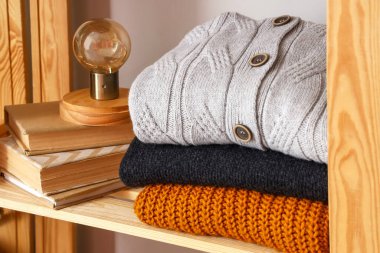 Kalın kazak, kitap ve lamba yığını, ışık duvarının yanındaki rafta, yakın plan.