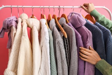 Pembe duvarın yanında kalın kazaklı kadın ve askılar, yakın plan.