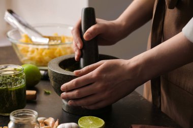 Kadın mutfaktaki masada havan ve tokmakla pesto sosu yapıyor.