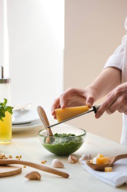 Mutfaktaki masada pesto soslu peyniri rendeleyen kadın.