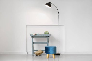 Işık duvarının yanında parlayan lamba, masa ve mavi pouf