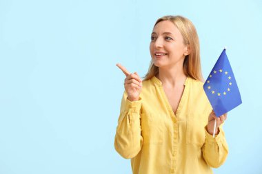 Avrupa Birliği bayrağı taşıyan olgun bir kadın renk arkaplanına işaret ediyor