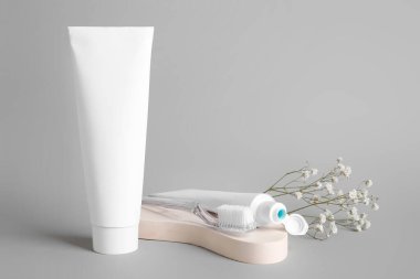 Gri arka planda diş macunu tüpleri, diş fırçası ve çiçeklerle kompozisyon