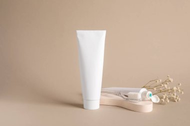 Bej arka planda diş macunu tüpleri, diş fırçası ve çiçeklerle kompozisyon