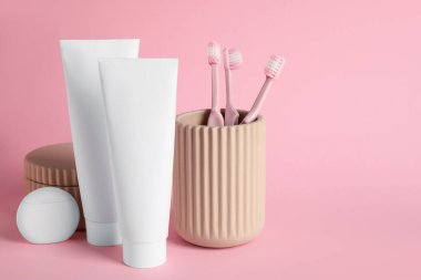 Diş macunlu tüpler, diş ipi ve arka planda diş fırçası olan tutucu.