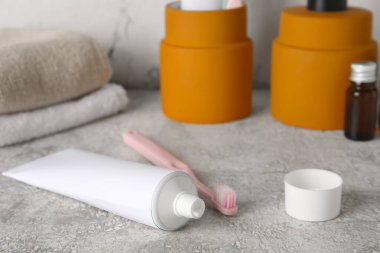 Gri masada diş macunu ve diş fırçasıyla açılmış bir tüp.