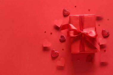 Sevgililer Günü hediyesi ve kırmızı arka planda dekoratif kalpler.