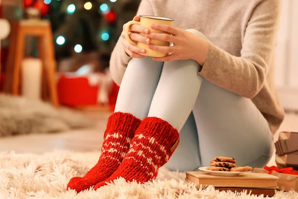 圣诞节前夕 穿着保暖袜子 杯子放在地板上的女人坐在家里 — 图库照片