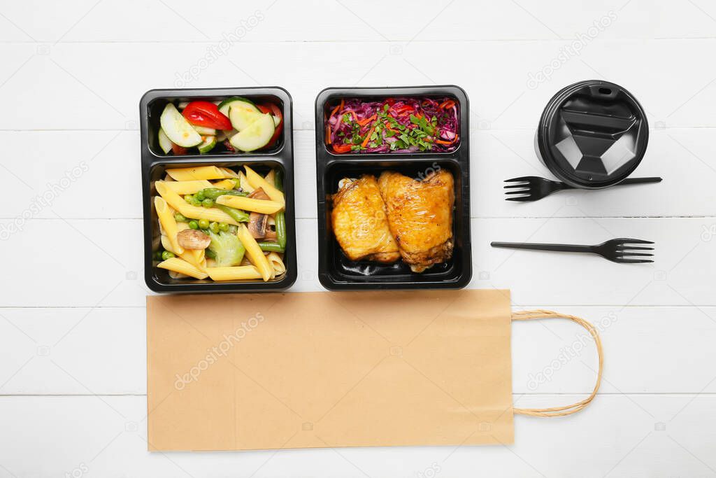 Lunch boxes with food, cup, forks and paper bag on white wooden background