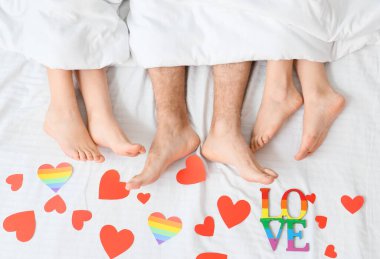 Genç bir adam ve iki kadının bacakları kağıttan kalplerle kaplı olarak yatıyordu. Çokeşlilik ve LGBT kavramı