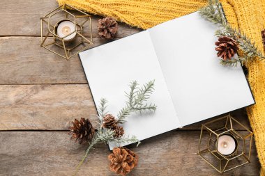 Boş sayfaları olan, köknar ağacı dalları olan ve ahşap arka planda mum yakan bir kitap.