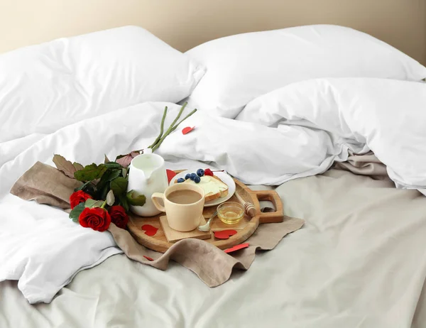 ベッドの上でバレンタインデーのためのおいしい朝食とバラの花束を持つ木製のボード — ストック写真