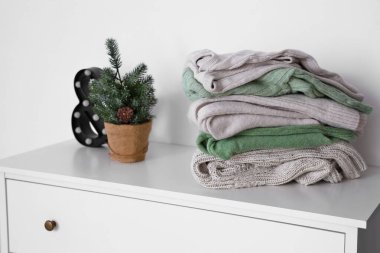 Sıcak süveter yığını, ışık duvarının yanındaki klozette küçük Noel ağacı ve dekor.