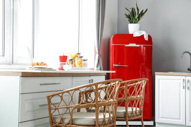 Kırmızı buzdolabı, beyaz tezgah ve hasır sandalyeli modern mutfak.