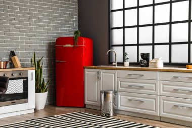 Kırmızı buzdolabı, beyaz tezgah ve pencereli şık bir mutfak.