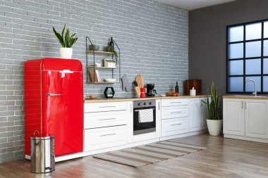 Kırmızı buzdolabı, beyaz tezgah ve tuğla duvarlı şık bir mutfak.