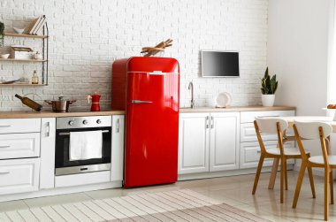 Kırmızı buzdolabı, beyaz tezgah ve yemek masası olan aydınlık mutfağın içi.