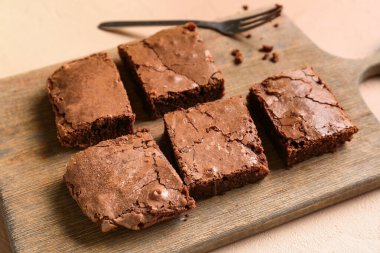 Bej arka planda lezzetli çikolatalı brownie parçaları olan ahşap tahta tahta, yakın plan.