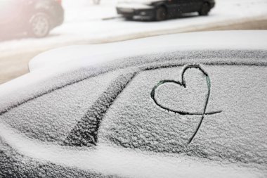 Açık havada karla kaplı arabaya kalp çizilmiş.