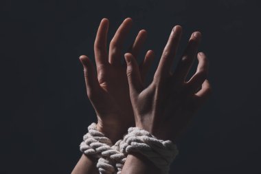 Karanlık arka planda rehinelerin elleri birbirine bağlı.