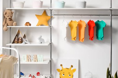 Oyuncak ve bebek kıyafetleriyle aydınlık çocuk odasının içinde.