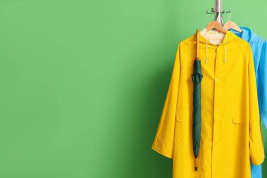 Yeşil duvarın yanında yağmurluklu ve şemsiyeli raflar