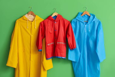 Yeşil duvarda asılı parlak yağmurluklar