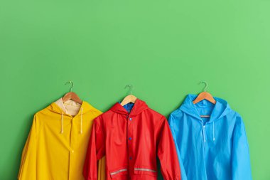 Yeşil duvarda asılı parlak yağmurluklar