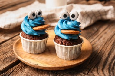 Cadılar Bayramı kutlaması için ahşap arka planda lezzetli, komik keklerle dolu tabaklar.