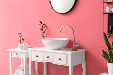 Pembe duvarın yanındaki vazoda lavabo, sabun ve bitki dalı olan masa.