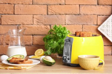 Tuğla duvarın yanındaki masada lezzetli kahvaltılı sarı ekmek kızartma makinesi.