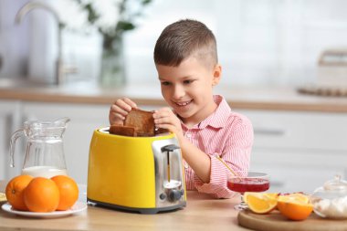 Sevimli küçük çocuk mutfaktaki sarı tost makinesinden ekmek dilimini alıyor.