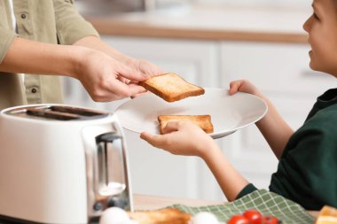 Annesiyle küçük bir çocuk mutfakta kızarmış ekmek dilimlerini tabağa koyuyor.