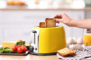 Mutfakta ekmek kızartma makinesinden ekmek dilimi alan bir kadın.