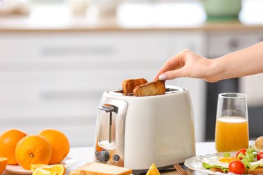 Kadın mutfakta ekmek kızartma makinesinden ekmek dilimi alıyor.