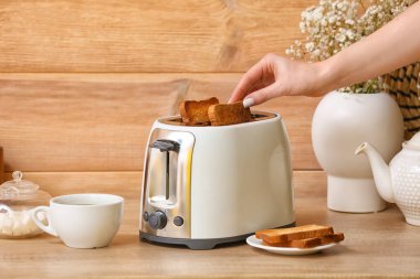 Ahşap duvarın yanındaki ekmek kızartma makinesinden ekmek dilimi alan kadın.