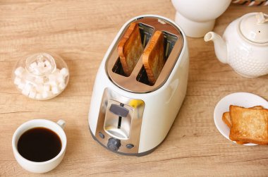 Beyaz ekmek dilimli tost makinesi, bir fincan kahve ve şeker kasesi ahşap masada.