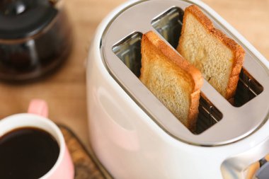 Ekmek dilimli beyaz tost makinesi ve masada bir fincan kahve, yakın plan.