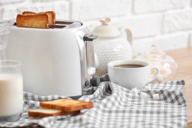 Tuğla duvarın yanındaki masada ekmek dilimleri ve içeceklerle beyaz ekmek kızartma makinesi.