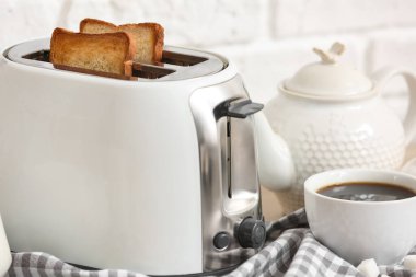 Ekmek dilimli beyaz tost makinesi ve masada bir fincan kahve, yakın plan.