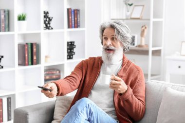 Evdeki kanepede kahve içip televizyon izleyen son sınıf öğrencisi.