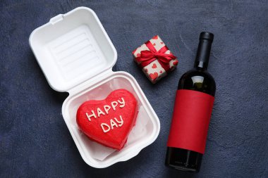 Esmer arka planda lezzetli bento keki, hediye ve bir şişe şarap olan plastik beslenme çantası.