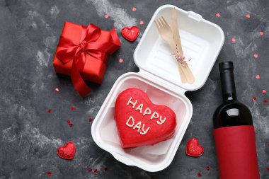 Esmer arka planda lezzetli bento keki, hediye ve bir şişe şarap olan plastik beslenme çantası.