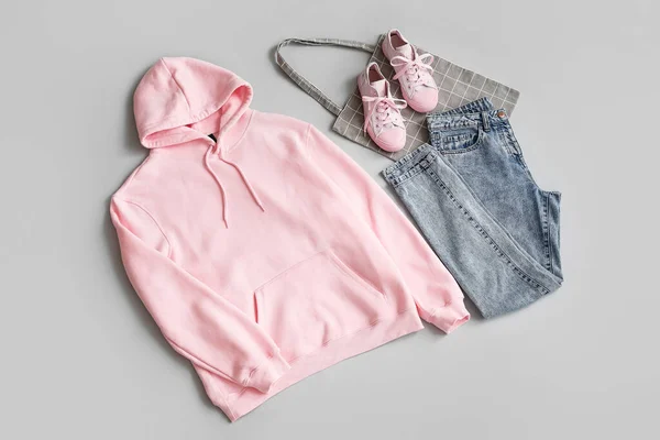 粉色帽衫 灰色背景的牛仔裤 运动鞋和购物袋 — 图库照片