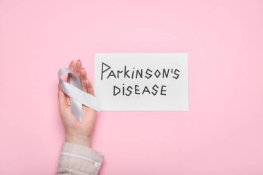 Parkinson hastalığı, kadın eli ve pembe arka planda farkındalık kurdelesi olan bir kağıt.