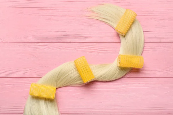 Žluté Natáčky Blond Vlasy Pramen Růžovém Dřevěném Pozadí — Stock fotografie