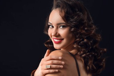 Koyu arka planda omzuna dokunan gülümseyen genç bir kadının portresi.