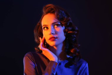 Yüzüne yakın eli olan kadın karanlık arka plana bakıyor.